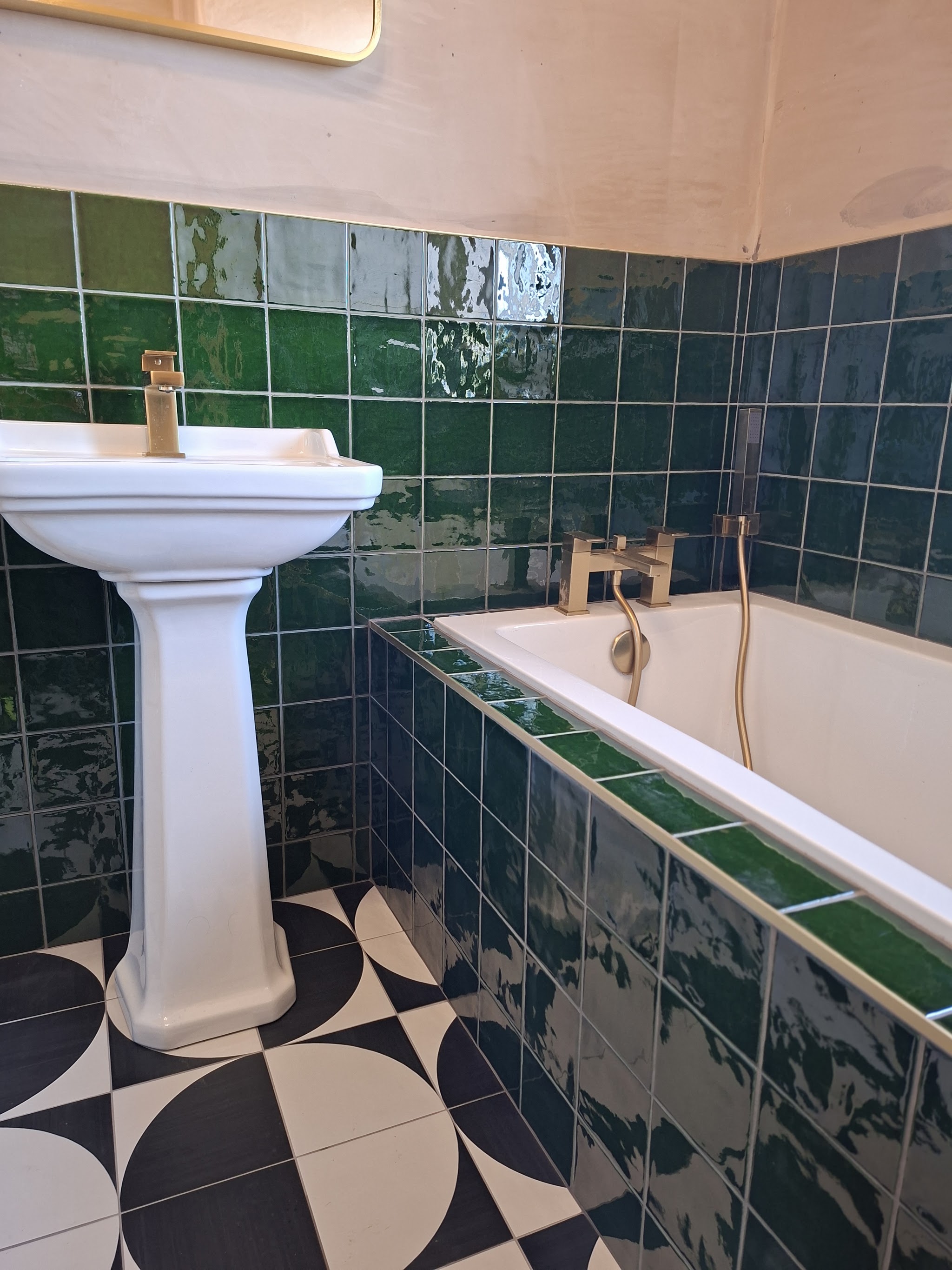 Glossy green bathroom wall tiles above a patterned black and white floor