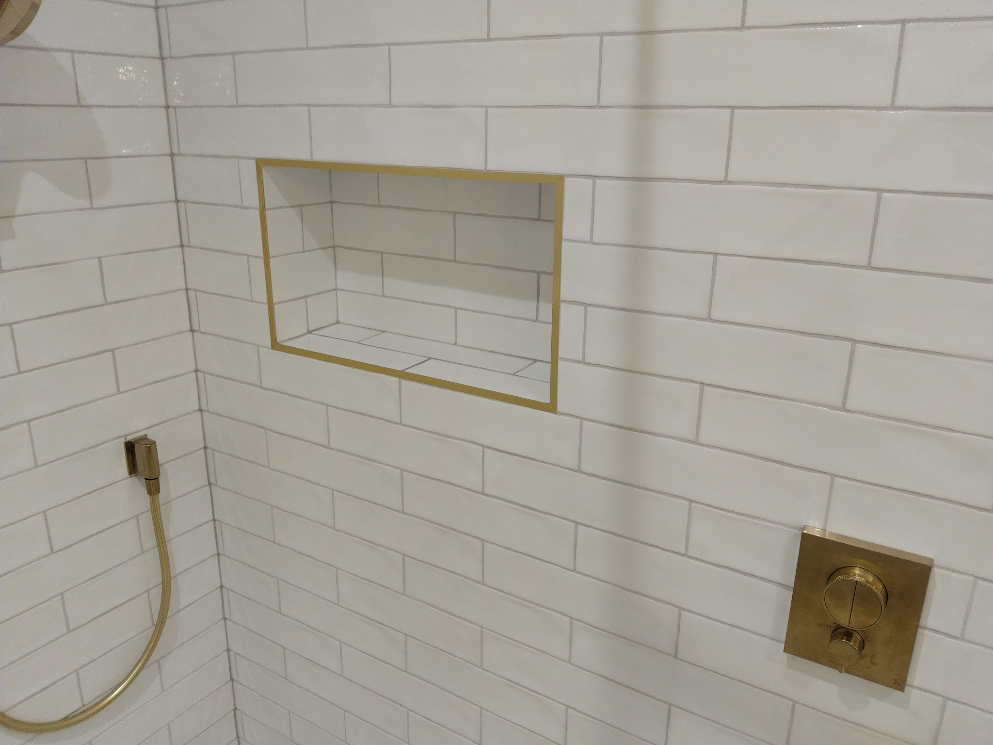 White brick tiles in a shower with brass fittings.